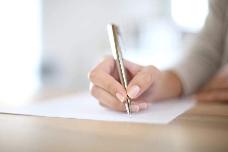 Woman's hand with pen and paper writing a life review